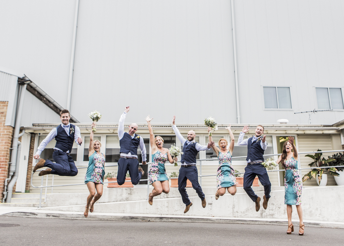 Bridal party jumping for joy in front of warehouse