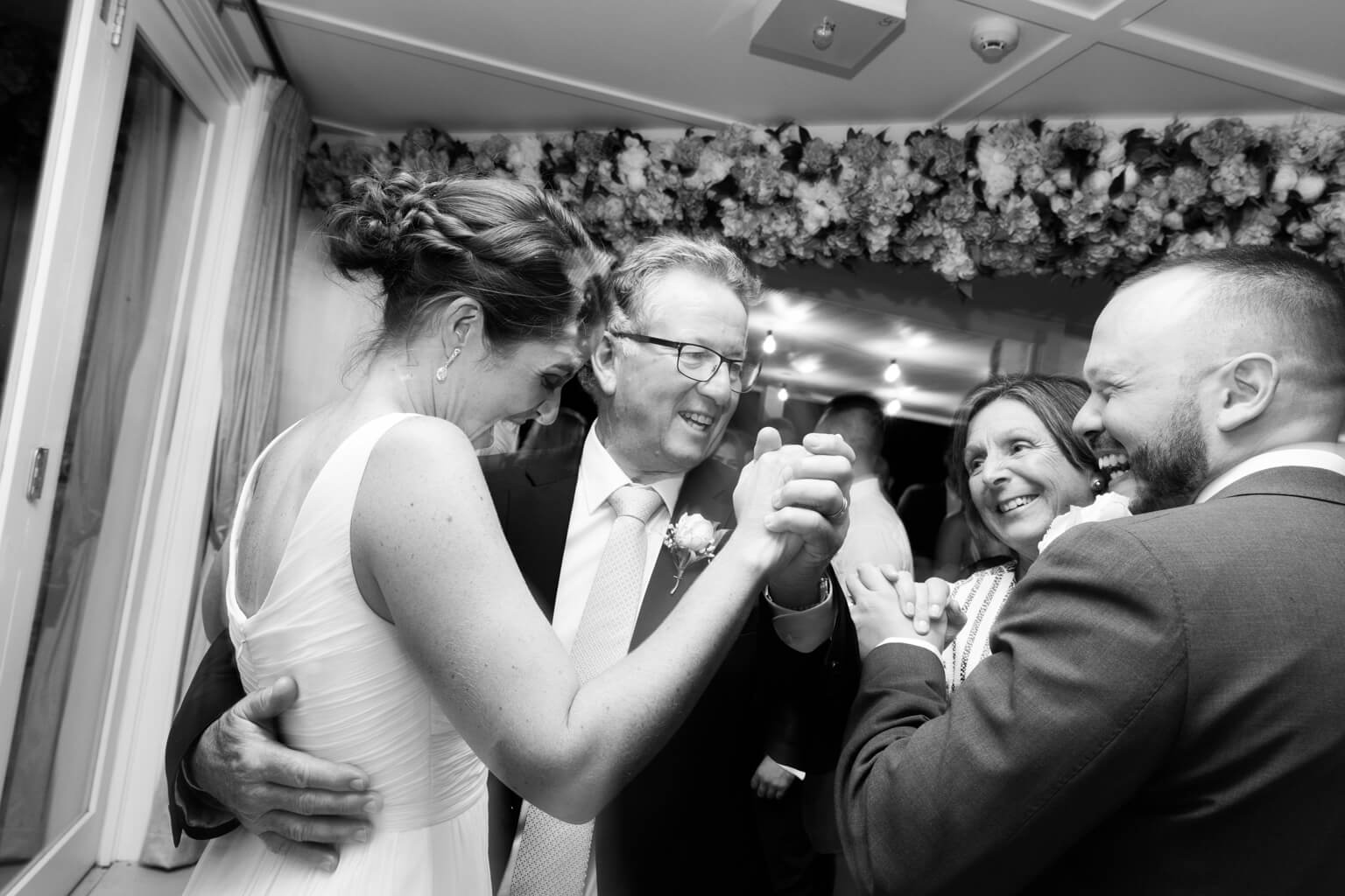 Bride and groom dancing wither her parents in black and white