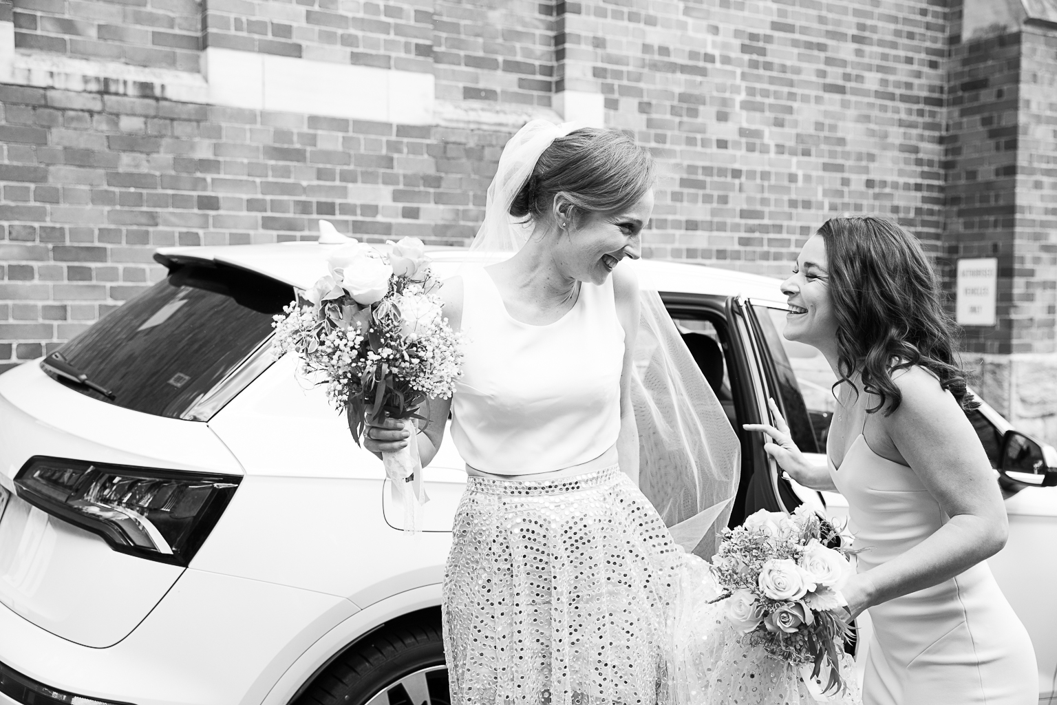 bride and matron of honour lasugh whilst getting out of the car at church